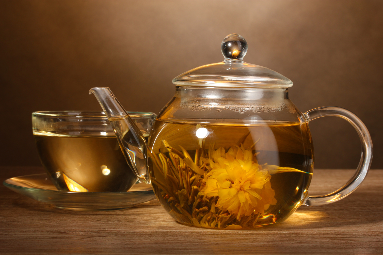 Glass Teapot and Cup with Exotic Green Tea on Wooden Table on Brown Background